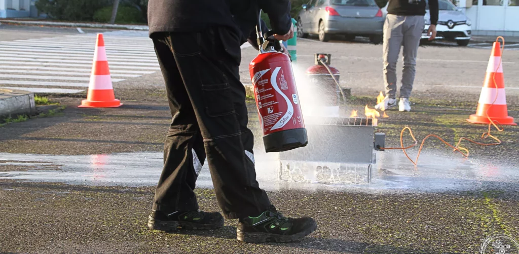 Un homme utilise un extincteur sur un bac à feu lors de formations sécurité incendie
