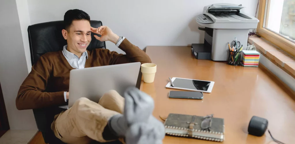 Un homme est très mal assis sur son poste de travail avec son ordinateur, il n'a pas optimisé son Ergonomie et poste de travail.