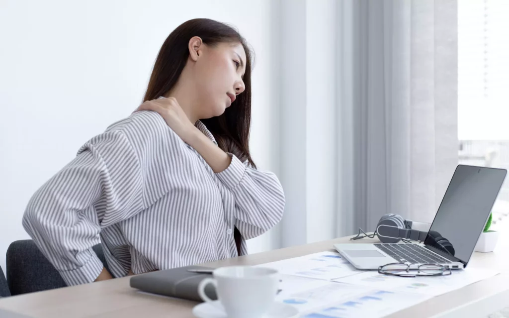 Une femme ressent des TMS devant son écran car l'Ergonomie de son poste de travail n'est pas optimisée